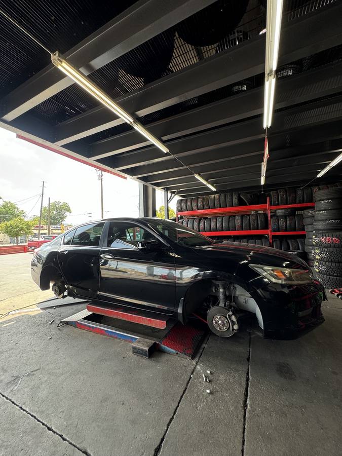 A sedan on the lift in the bay, alongside a wall of new tires on red racking.