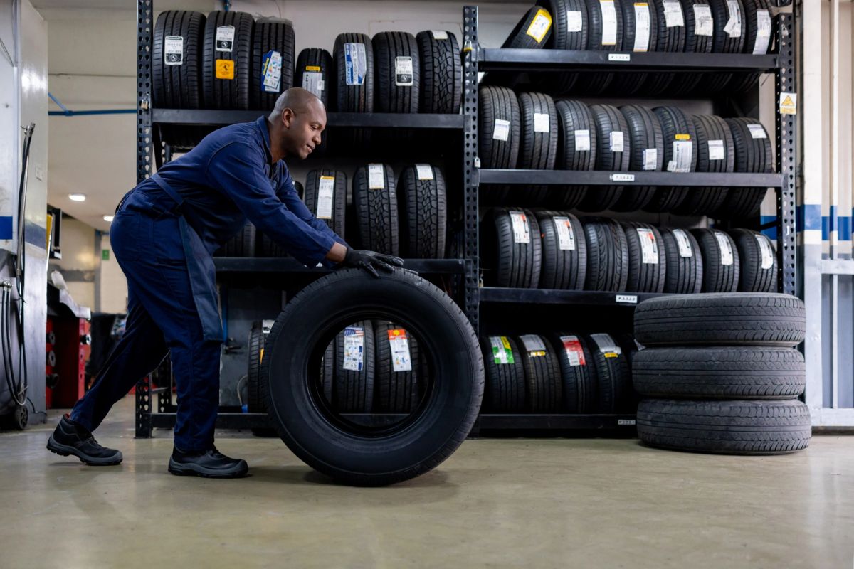 A mechanic changing a flat tire and carrying a wheel at a repair garage.