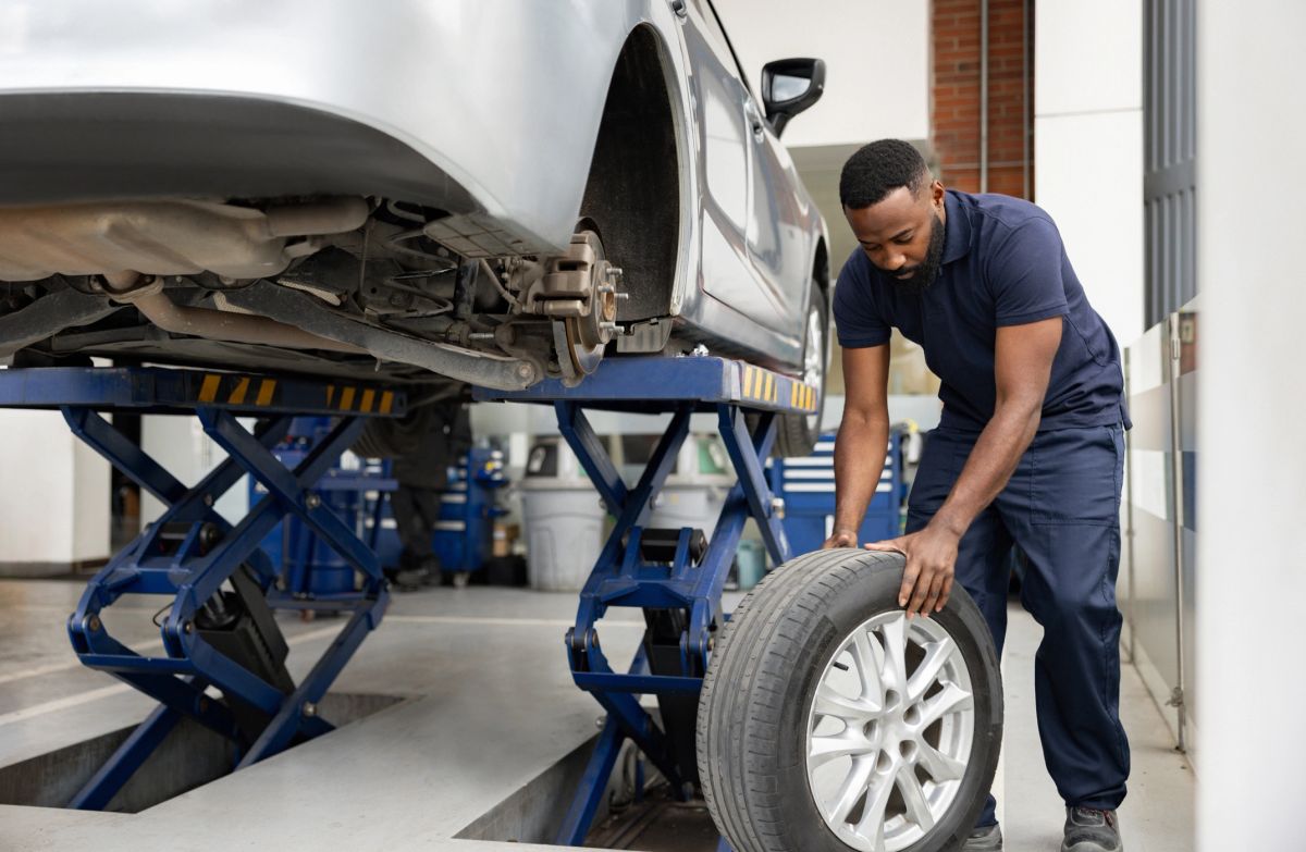 A mechanic changing a flat tire on a car at a garage.