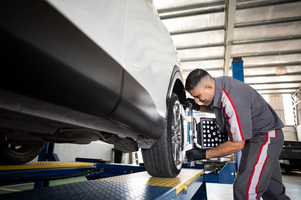 A technician checking wheel alignment on a lifted vehicle in a shop.