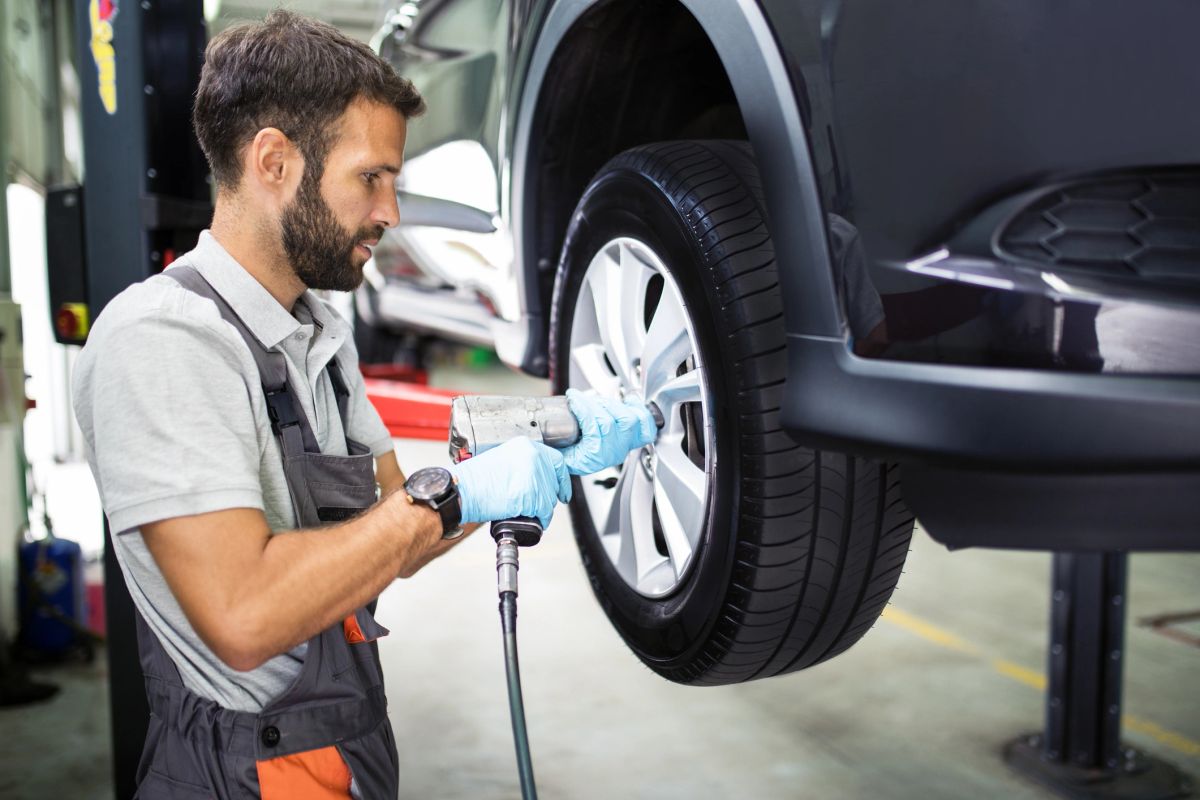 A mechanic using an impact wrench on a vehicle wheel in a shop.